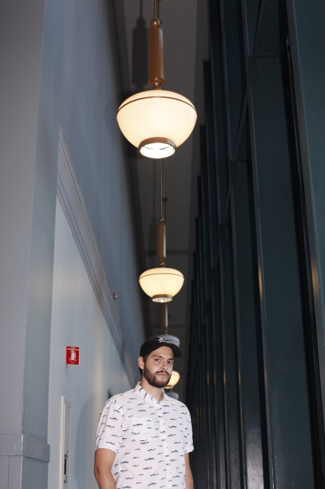 A man standing in a tall hallway under a row of hanging globe lamps