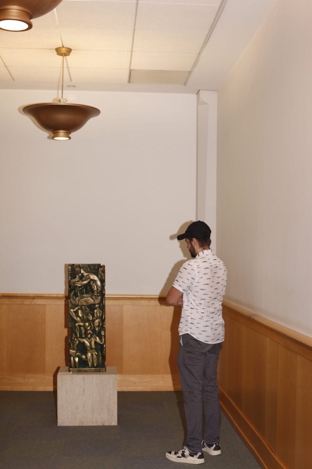 A man studying a bronze sculpture on a stone plinth in a quiet gallery